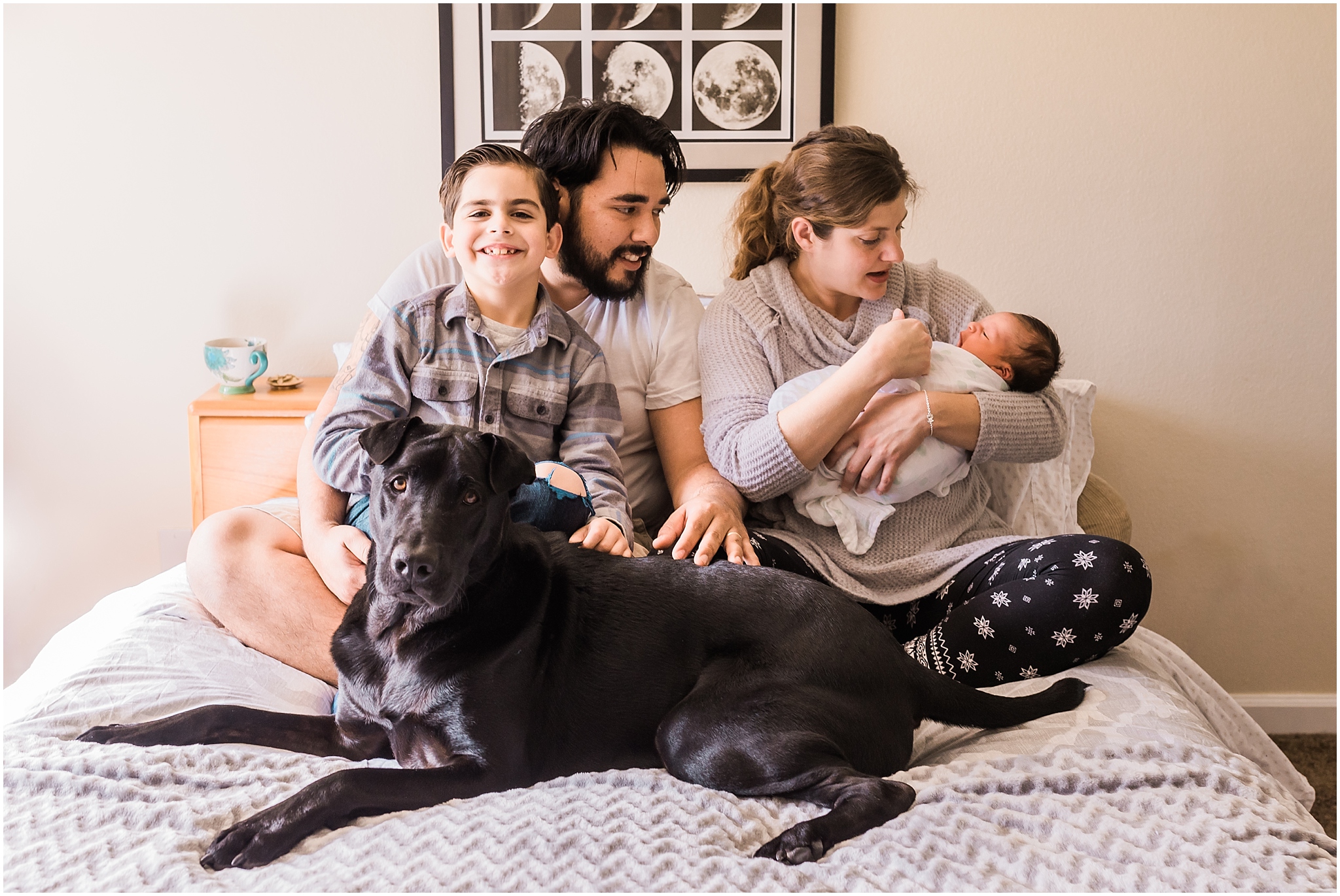 Family with newborn baby and dog on bed