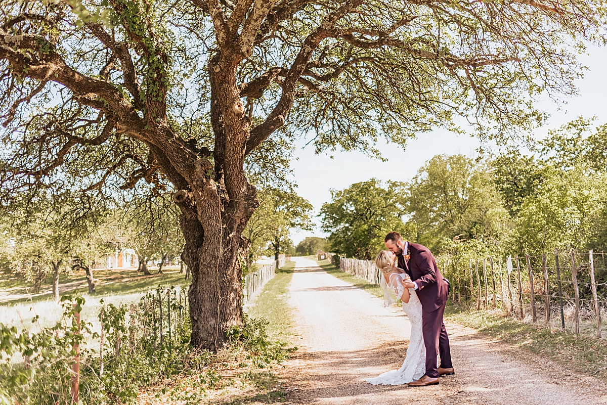 groom dipping bride for a kiss on a dirt path under a large tree