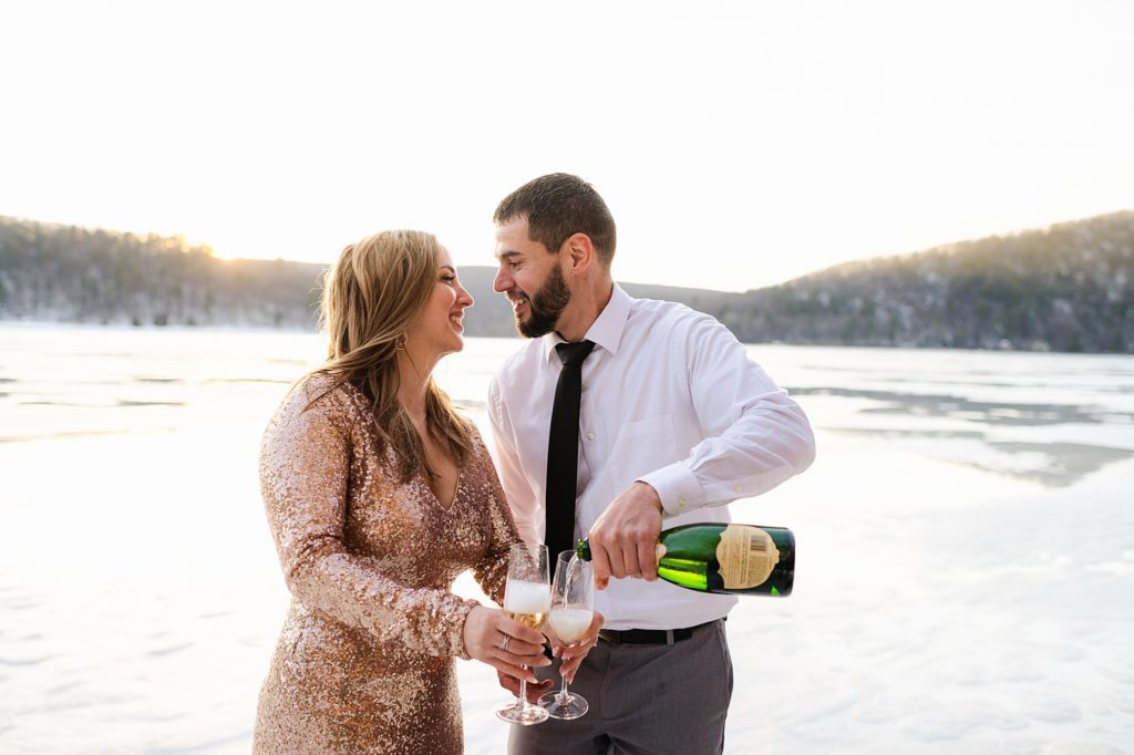 popping champage at an engagement session on a frozen lake