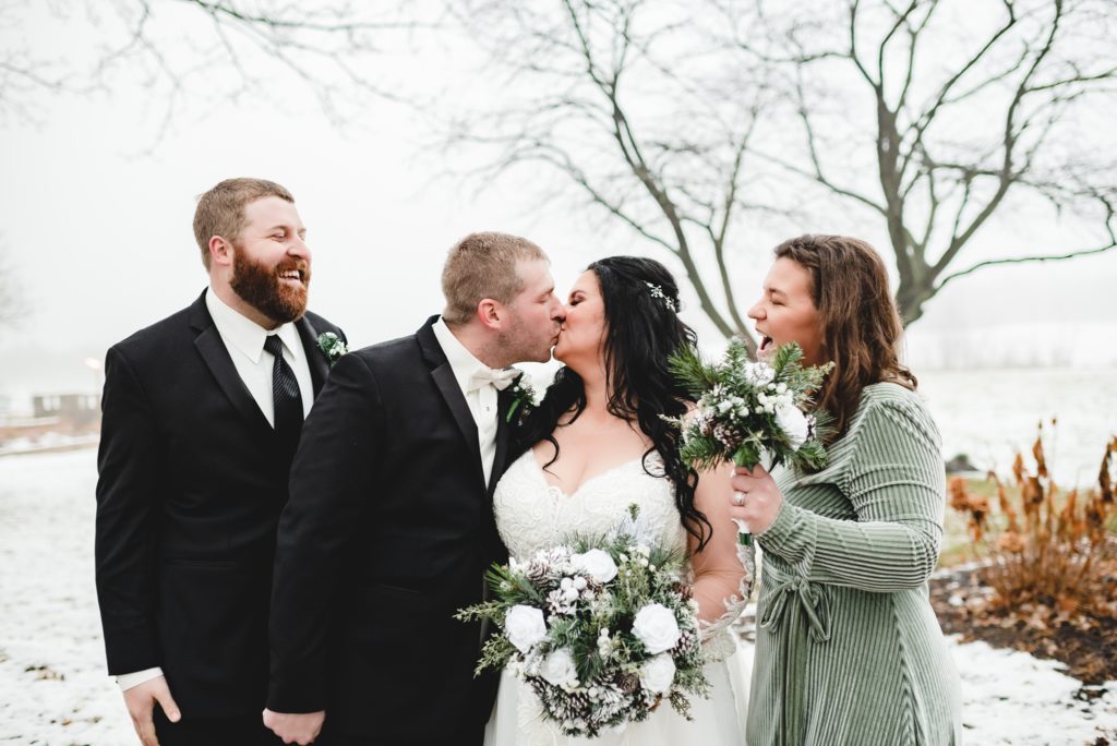 bride and groom kissing with best man and maid of honor watching