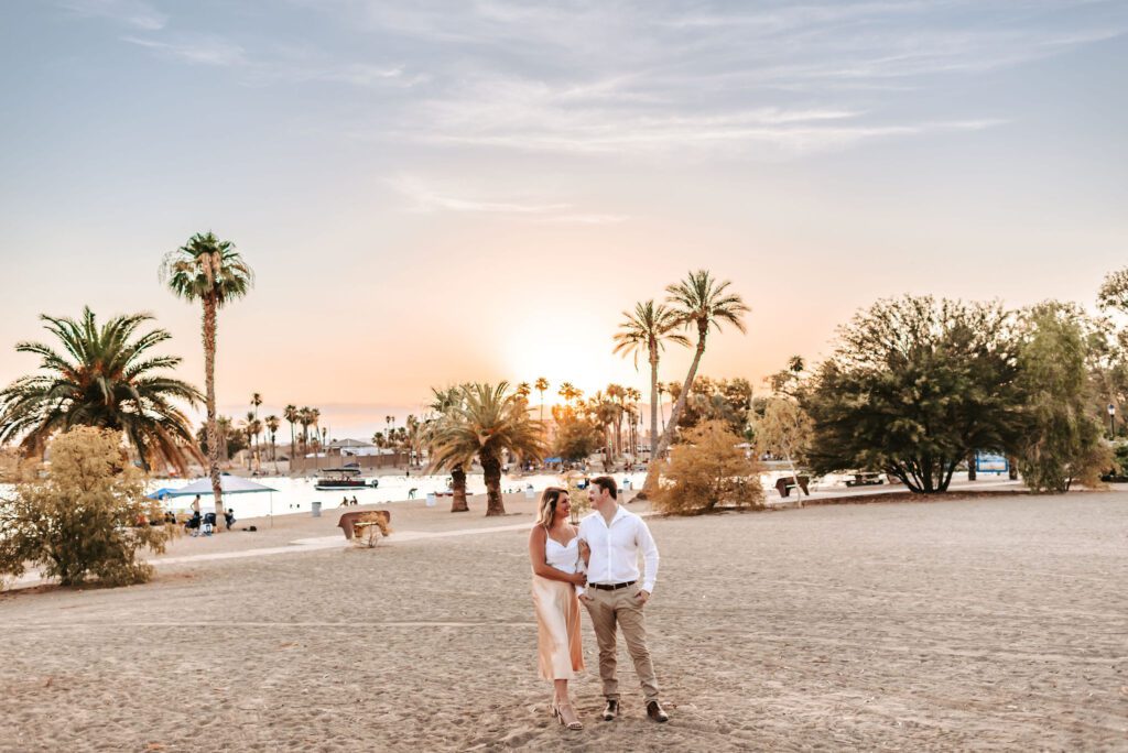 engaged couple kissing with palm trees and sunset behind them
