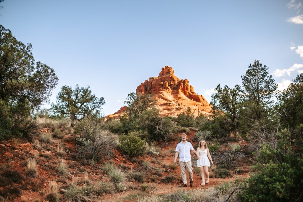 couple walking together with bell rock sedona behind them