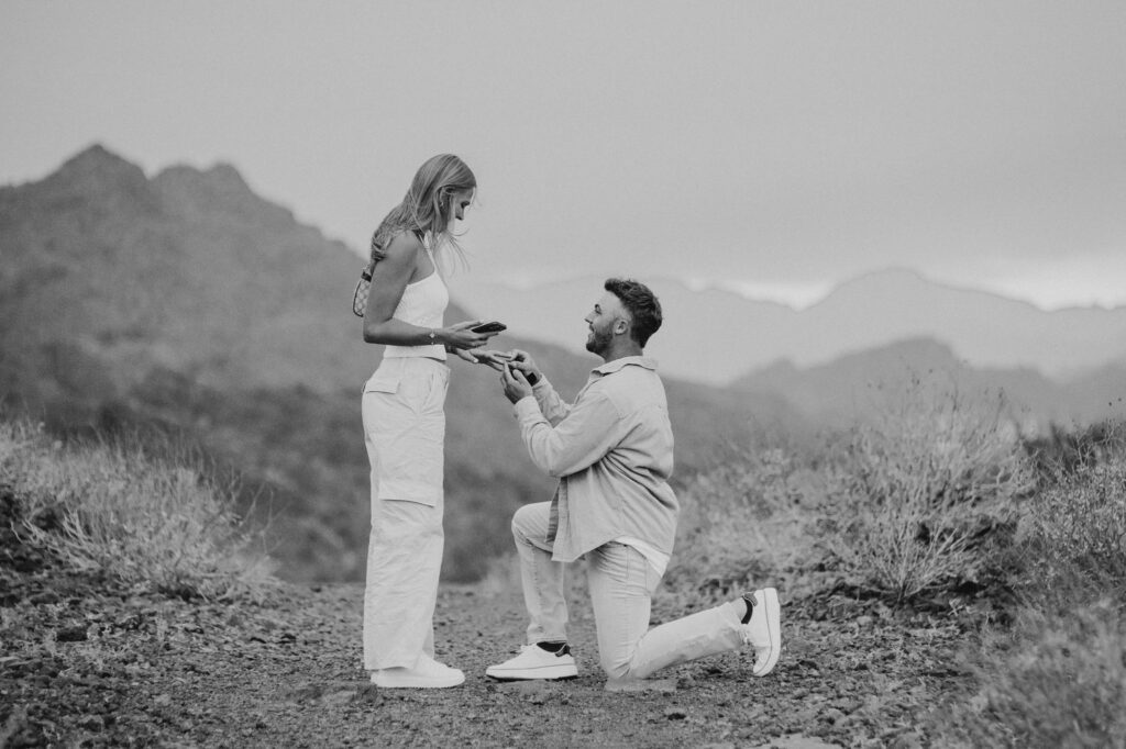 man on one knee, proposing to girlfriend at sunset with mountains in the background