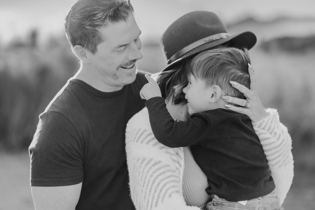 mom hugging toddler son while dad smiles at son