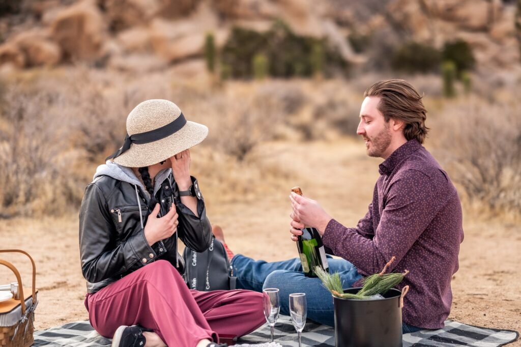 man pouring glass of champagne at engagement picnic