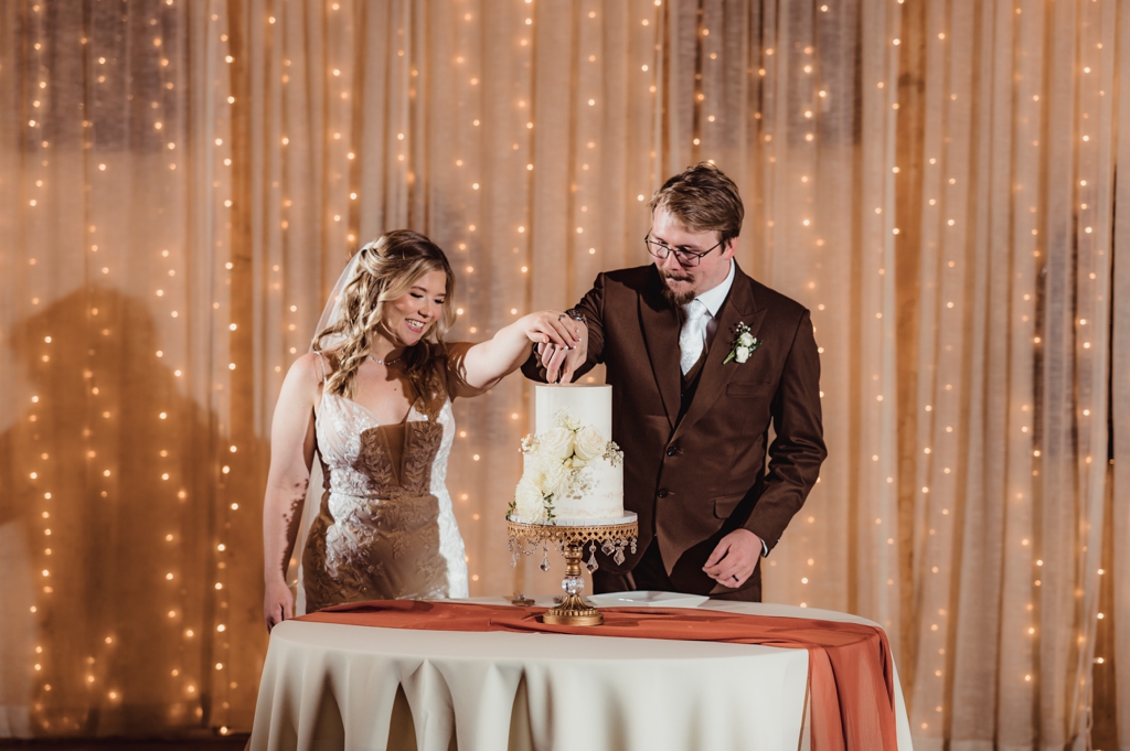 newlyweds cutting cake in front of string light curtain