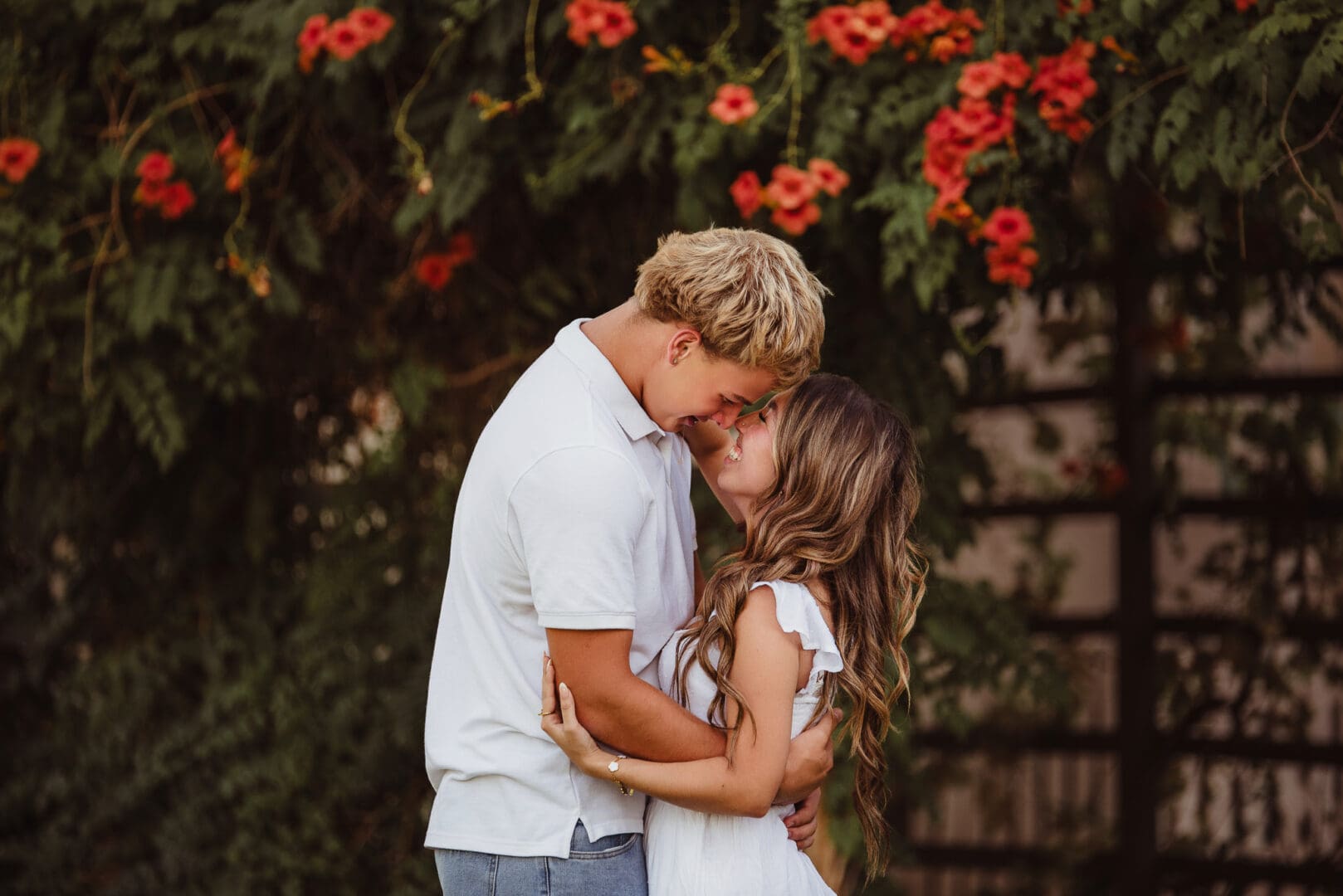 high school sweethearts embracing in front of hibiscus flowers