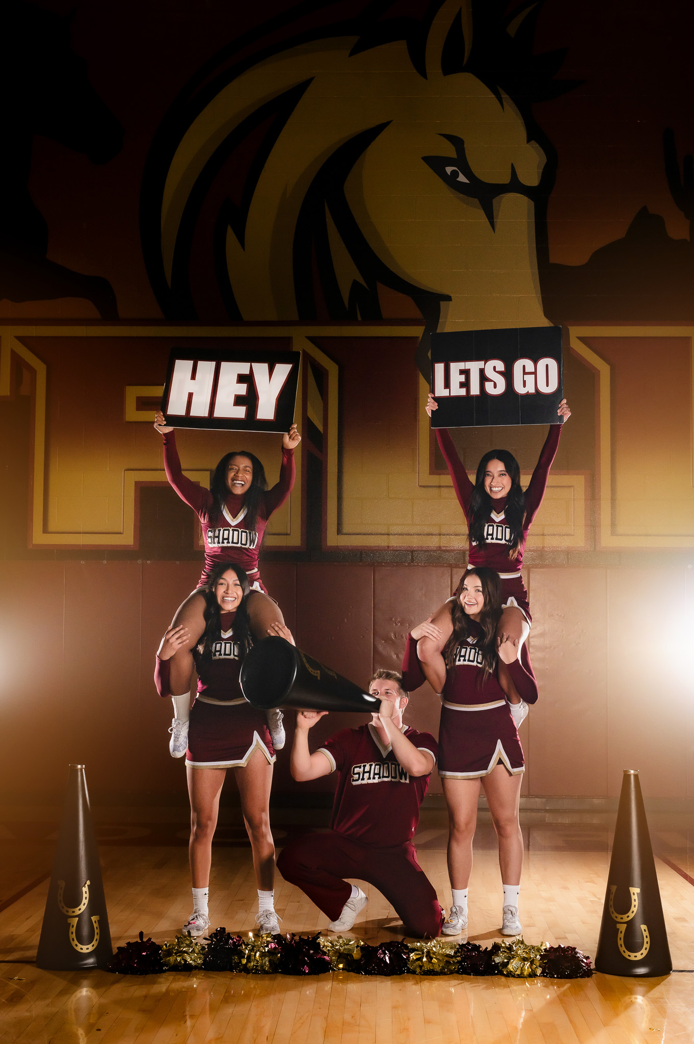 Group of five high school cheerleaders with signs sitting on each other's shoulders