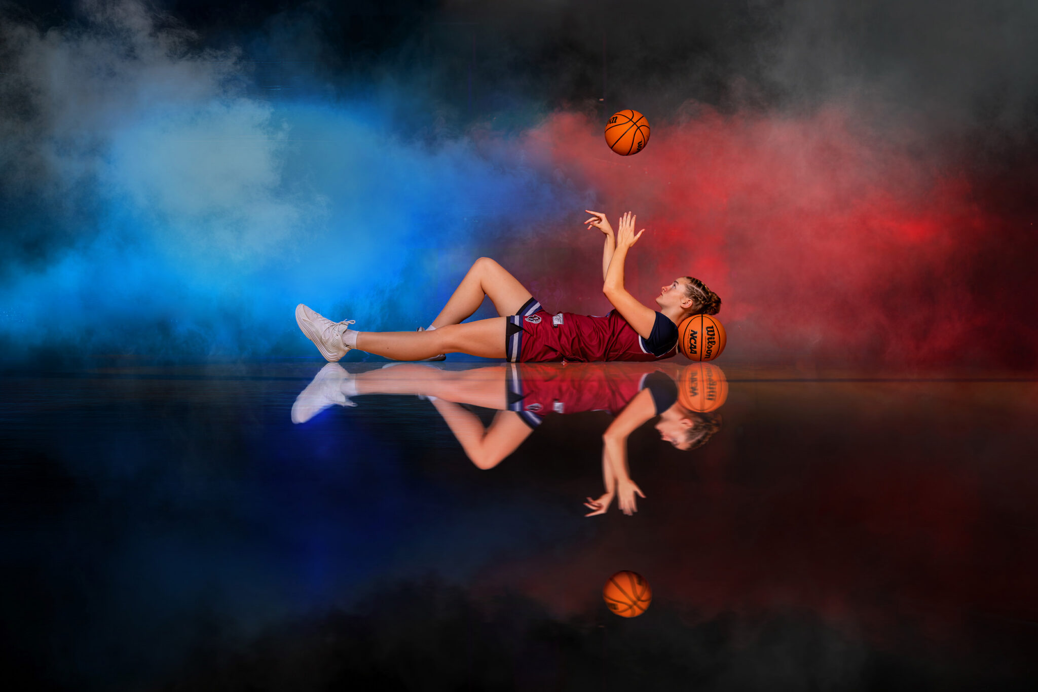 girl basketball player laying on gym floor tossing the ball with colored smoke behind her