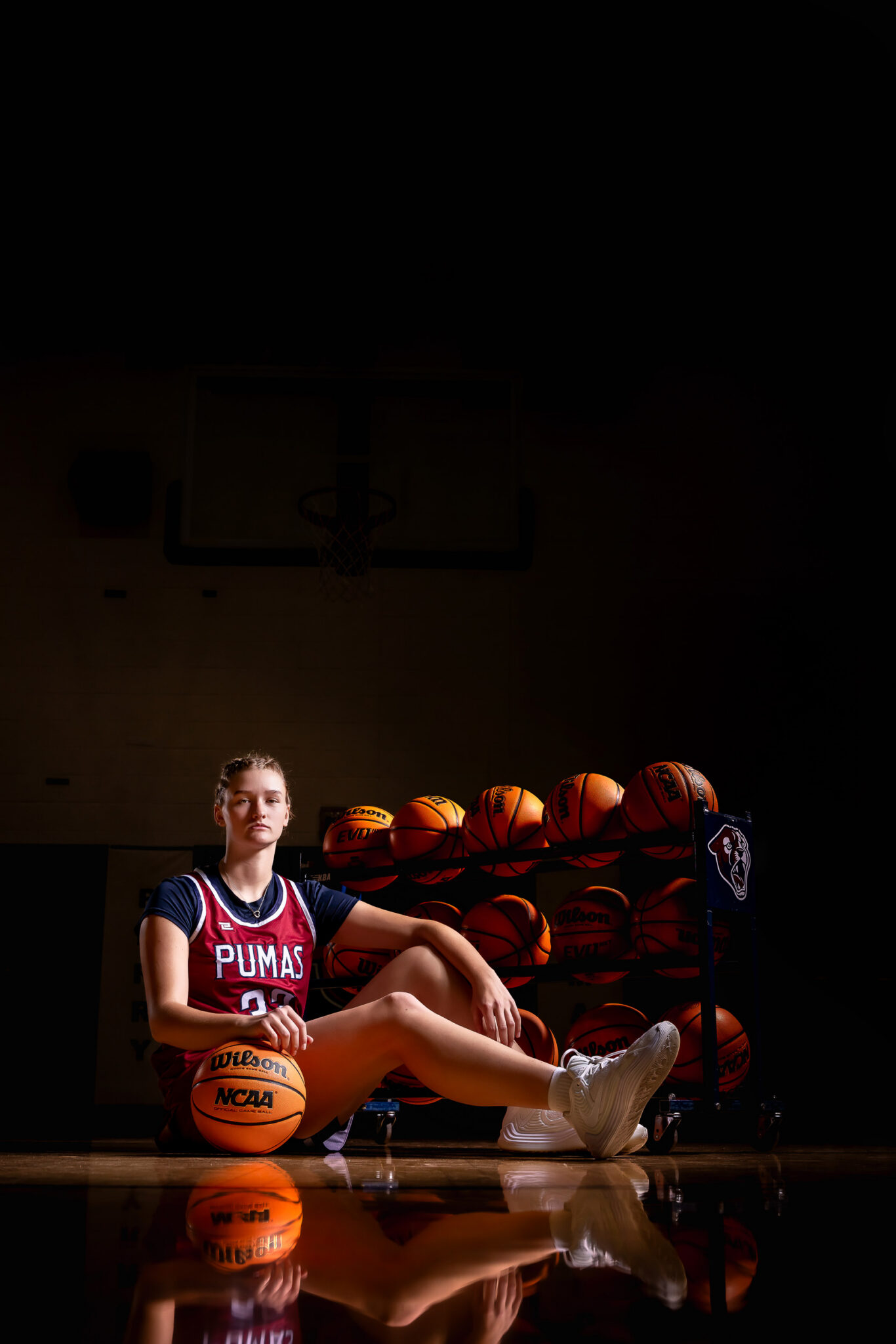 Female athlete senior portrait featuring dramatic lighting inside the gym