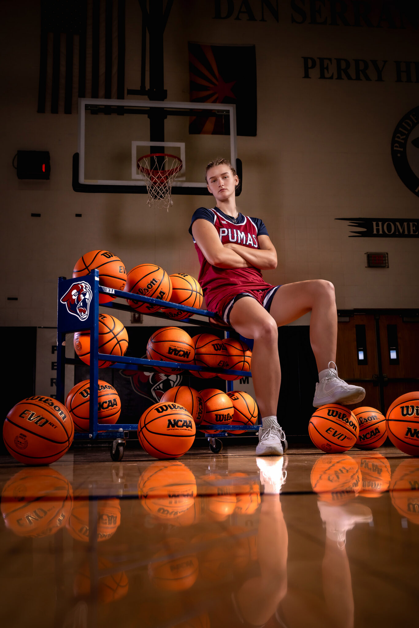 Female high school basketball player leaning on basketball cart under the gym lights at Perry High School