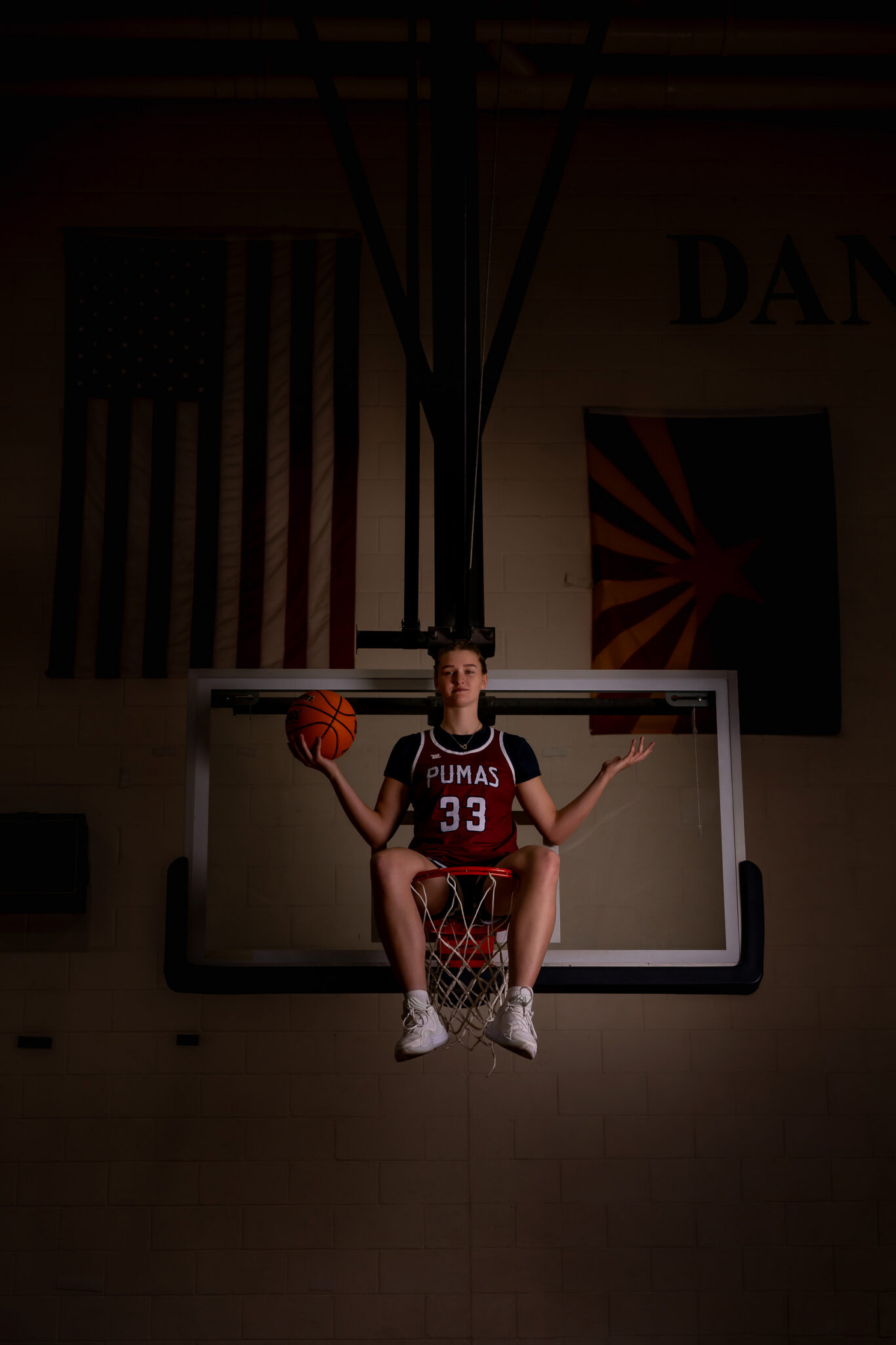 senior girl basketball player sitting on the basketball hoop