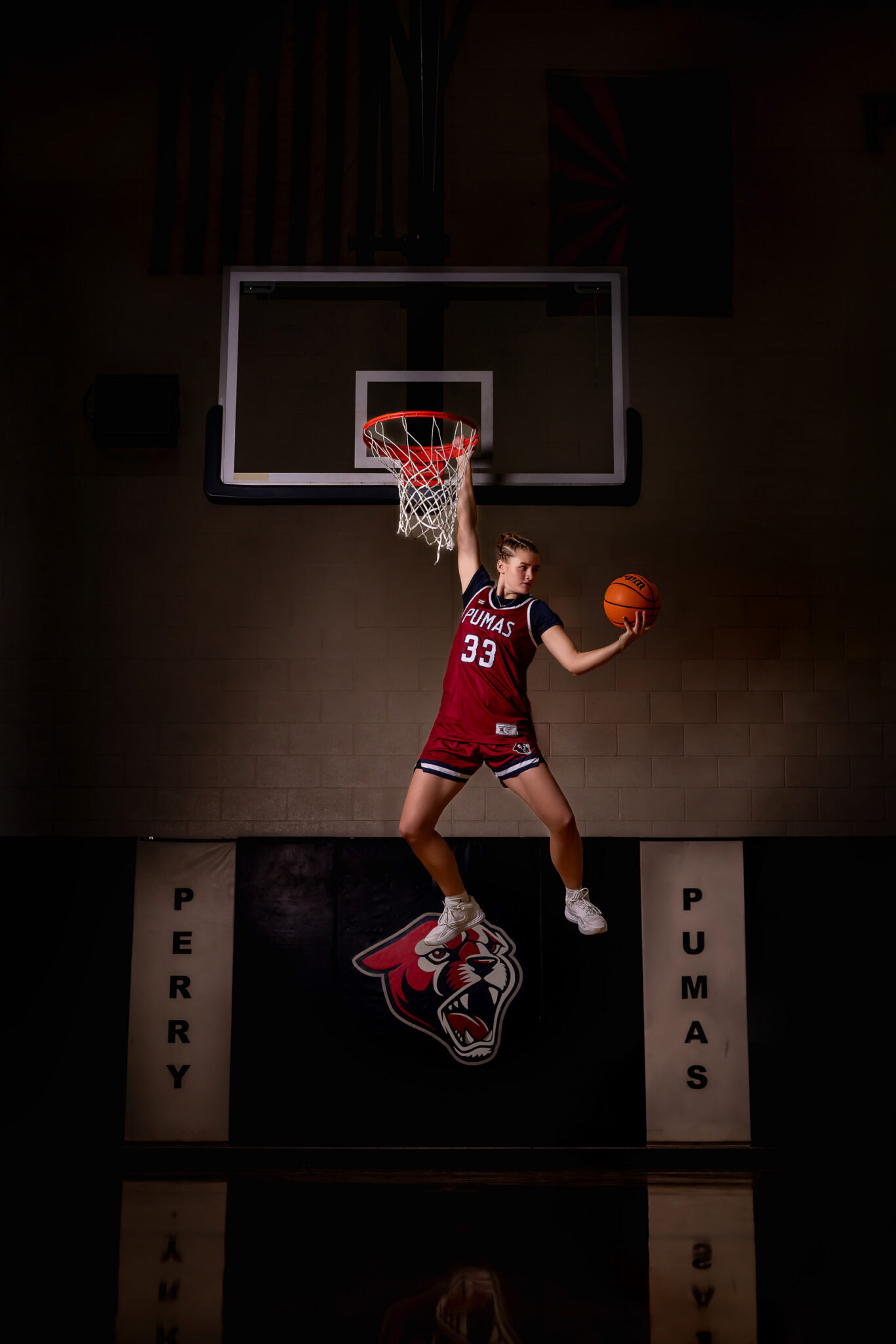 senior girl hanging off hoop with a basketball